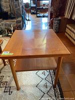 Front angled view showing the teak table top, rounded tapered legs, and the lower shelf beneath.