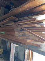 Long stacked boards of varying thickness and length, primarily reddish-brown teak.