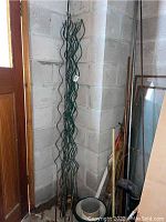 Full view of wire plant stakes bundled together leaning against a wall with 3 small plant pots seen on the floor