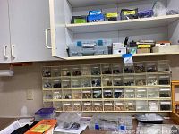 Wide view of large organizing cabinet with many labeled plastic drawers filled with clock making parts and smaller containers on top and below the cabinet