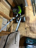 Electric cultivator on wooden shed floor showing handle, wheels, and power cord