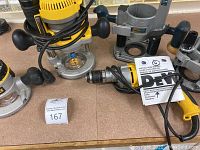Assorted power tools on countertop including Dewalt router motor with cord and base pieces, Dewalt drills, Dremel router attachment and other tools