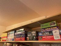 Photo of multiple stacked jigsaw puzzles on a wooden shelf showing variety of brands and piece counts.
