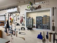 Wall section with saws, clamps, levels, wrenches, hammers, brushes and work light hanging under air conditioning unit