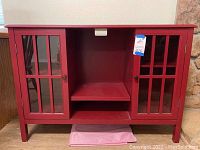 Front view of red wooden TV cabinet with both glazed doors closed, showing top surface and open center compartment
