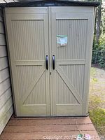 Full front elevation of beige Rubbermaid shed with two doors and black handles