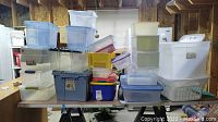 An assortment of plastic storage containers in various sizes, colors, and shapes stacked on a table.