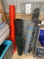 Photo showing multiple rolls of fencing including galvanized circular wire fencing, green coated wire mesh, chicken wire, and black roofing underlayment material alongside orange safety fencing.