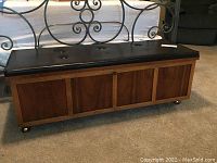 Front view of mid-century cedar chest with wood paneled sides and tufted black vinyl top.
