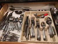 Drawer with multiple stainless steel knives, forks, spoons and serving utensils in two sections, one with loose items and one with organized flatware.