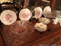 Overview of the porcelain and cranberry glass items, displayed on wooden cabinet with multiple plates and bowls arranged.