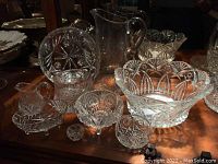 Multiple cut and pressed crystal bowls and a pitcher displayed together on a wood surface. Includes large and small bowls with detailed cut patterns.