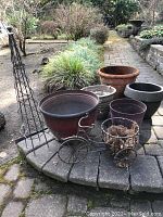 Photo showing the group of five resin pots of different sizes and colors with the black metal topiary frame and bicycle planter on a stone patio.