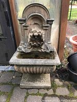 Front view of garden fountain showing two-piece stone statuary with basin and arched back panel with decorative spout.
