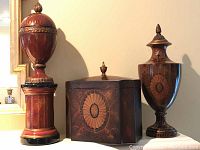Photo shows three pieces: two lidded urns of different sizes and shapes, and one rectangular hinged box between them, all with wood grain painted finish and decorative designs.