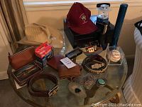 Overview of entire lot on glass table showing buckles, belts, hat, tools, and accessories