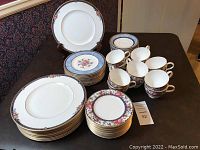 Full view of four stacks of plates and cups and saucers arranged on table showing floral china pattern and gold trim.