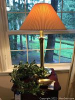 Full view of the brass Stiffel table lamp with pleated shade, vintage brass duck, and faux ivy on a wooden side table near a window.