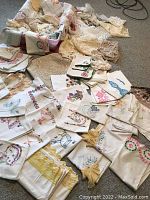 Photo showing a variety of embroidered pillowcases, lace pieces, and crocheted linens arranged on carpet.