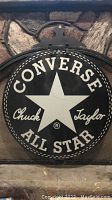Front view of round black and white Converse Chuck Taylor All Star metal sign showing the large white star and text on black background.
