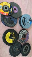 Seven assorted cutting, grinding, and sanding wheels laid on a flat surface showing brand labels and physical condition.