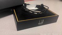 Photo showing Dunhill bracelet in black leather and silver-tone metal clasp resting in original Dunhill London box with black and gold trim.