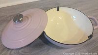 Open view of the pink enameled cast iron dish showing the cream-colored interior and lid with stainless steel handle.