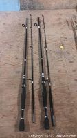 Two black fishing rods laid flat on a wooden surface showing full length with foam grip handles and metal guides.