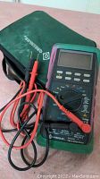 Greenlee DM-620 digital multimeter showing front face with rotary dial, buttons, test lead ports, and connected red and black test leads coiled on top.
