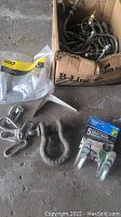 Photo showing box of metal U-bolts, metal clamps, large metal shackle, white bracket, and pack of metal utility hooks.