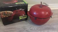 Photo showing the red apple-shaped Lodge cast iron enamel pot next to its original box.