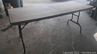 Photo of plastic folding table with visible paint marks and scratches on top, fully set up in garage floor area