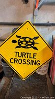 Yellow diamond-shaped turtle crossing sign with black turtle graphic and text, showing some minor wear and mounting holes.