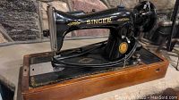 Side view of the black Singer sewing machine with gold detailing mounted on wooden base showing full machine.