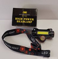 Photo of the boxed high power headlamp with elastic, printed LED headlight strap on white background.