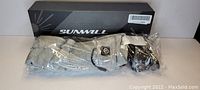 Photo showing light gray Sunwill heated socks with battery packs on top, inside plastic packaging, with the Sunwill branded box behind them.
