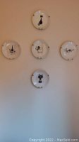 Five decorative plates mounted on wall showing various black and white cartoon cat illustrations by Albert Dubout.