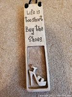 Vertical ceramic wall plaque with inscription and shoe sculpture detail.