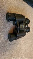 Photo of black binoculars with lens caps placed on a carpeted floor.