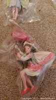 Close-up image of a fairy ornament holding a pink flower, wearing a pink and green dress with wings, still in plastic wrap.