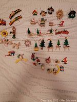 Full layout showing all 38 assorted wooden Christmas ornaments arranged in groups on a white cloth background. Items include trees, Santas, angels, toy train, nutcracker, rocking horse, and more.