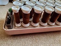 Full-size heated curlers with brown fabric rollers and white caps in pink heating base, includes metal clips