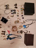 Full overview of jewelry items displayed on a beige cloth background, showing statement necklaces, earrings, two jewelry boxes, and assorted small jewelry pieces.