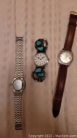 Photo showing three men's wristwatches: one with silver metal band, one with brown leather strap, and one with turquoise stone decorated band.