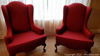 Pair of wine red wingback chairs placed side by side showing overall design and shape.