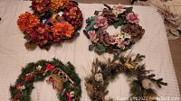 Top-down view of 4 seasonal wreaths on a light-colored surface including autumn, spring, Christmas, and woodland themes.