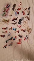 Full view of 29 shoe-shaped Christmas tree ornaments laid out on beige fabric, showing many colors and styles.