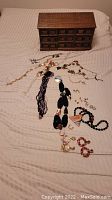 Photo showing wooden jewelry box and various necklaces and earrings spread on a bed