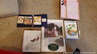 Shows various assorted stationery paper sets and matching envelopes, with diverse designs mostly floral and seasonal themed, arranged on carpet floor.