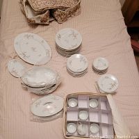 Overall assortment of fine china including stacks of plates, saucers, teacups, and serving dishes on a fabric surface.